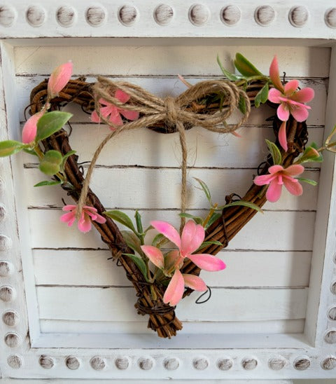 Heart-shaped wreath with pink flowers and twine on a white wooden background
