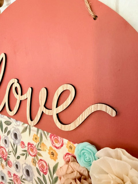 Wooden 'love' sign on a coral background with floral decorations.