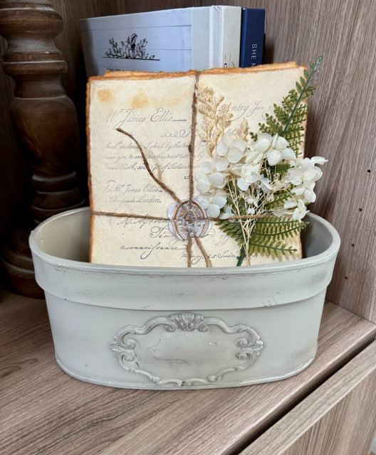 Decorative container with vintage book, flowers, and a small plant on a wooden surface.