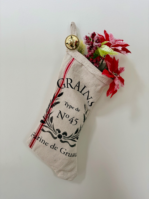 Cream decorative stocking with black stencil and red poinsettias.  Gold bell hangs from the top.