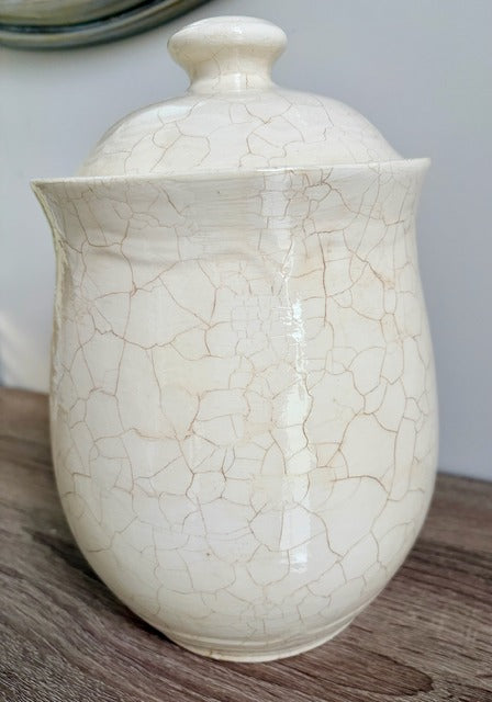 White ceramic canister with a cracked glaze finish on a wooden surface.