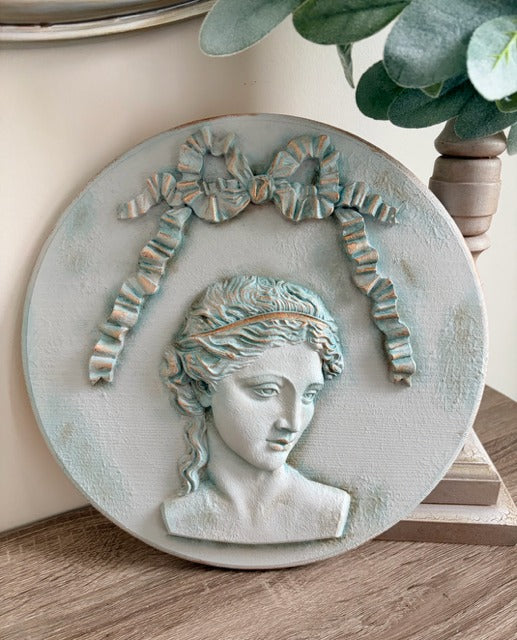 Decorative wall plaque with classical bust design on a wooden surface.
