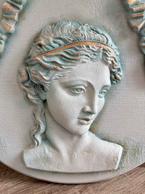 Decorative wall plaque with a classical bust design on a wooden surface