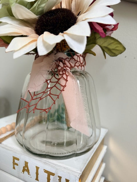 Clear glass vase with embroidered pink ribbon and flowers on a white surface