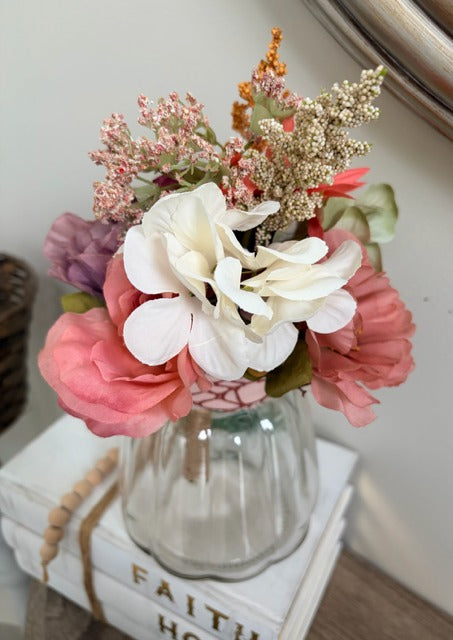 Bouquet of flowers in a glass vase on top of books with a blurred background