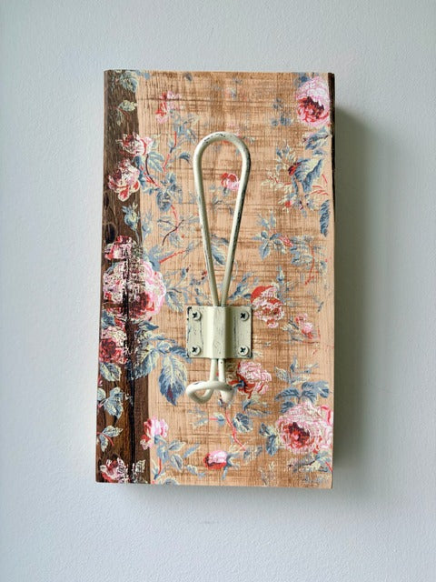 Decorative wall hook with floral pattern on a wooden board against a light gray background