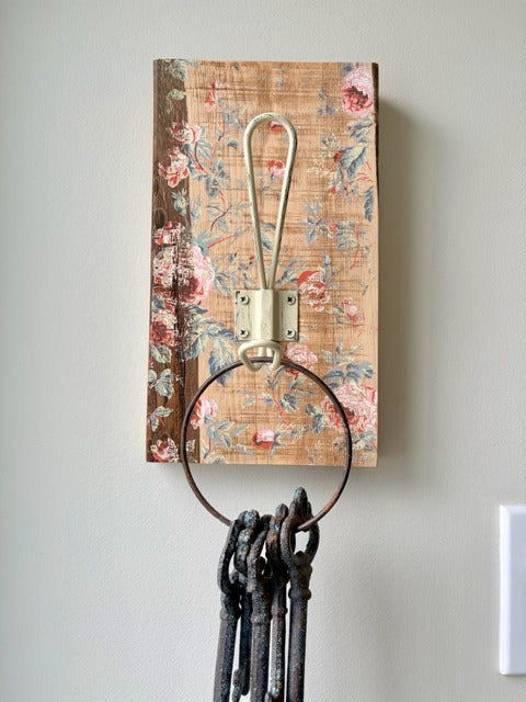 Decorative wall hook with floral-patterned board and metal hooks on a plain wall.