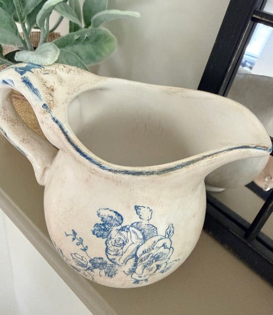 Vintage-style ceramic pitcher with blue floral patterns on a surface.