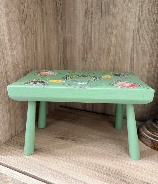 Green children's stool with floral design on a wooden floor.