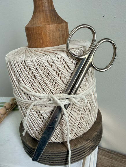 Spool of beige thread with a pair of scissors on a wooden spool against a white background