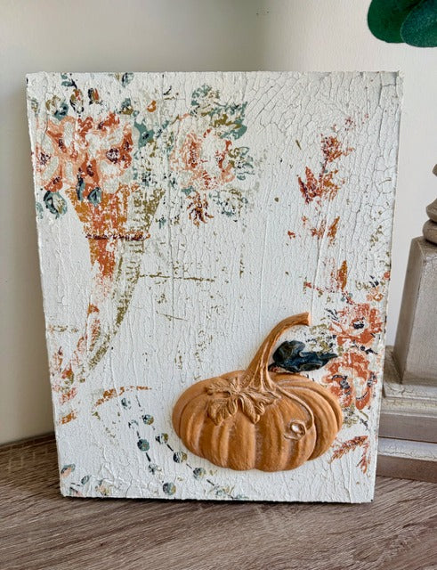 Decorative wall art with a pumpkin and floral design on a textured surface.