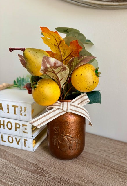 Decorative arrangement with pears and leaves in a copper jar on a wooden surface.