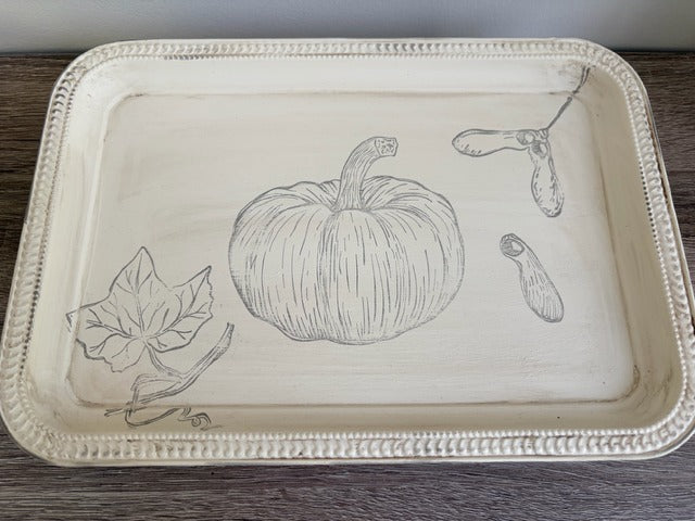 Decorative tray with black line art of a pumpkin and leaves on a wooden surface