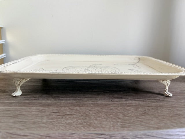 Decorative white metal tray with embossed design on a wooden surface