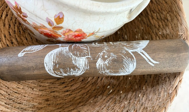 Wooden rolling pin with apple design on a woven surface