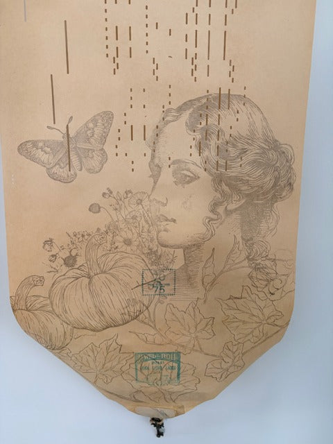 Paper wall art with stamped design of a woman's face, flowers, and a butterfly on a beige background.