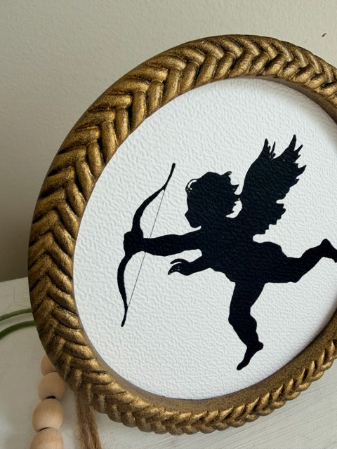 Silhouette of a winged archer in a gold-framed circular artwork on a white background