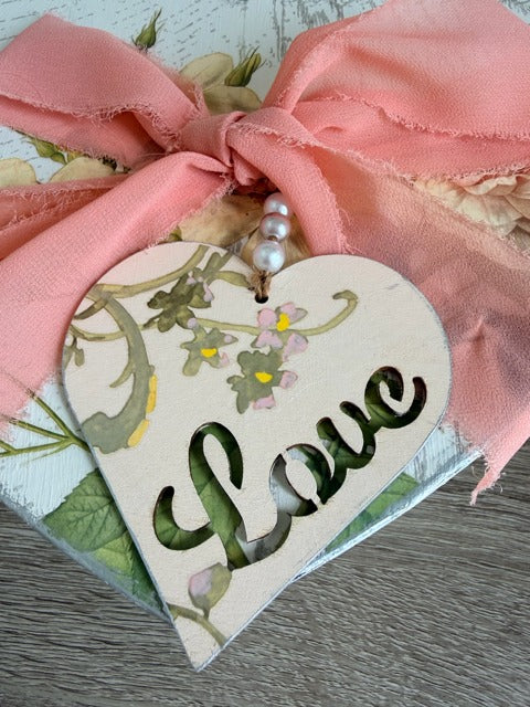 Heart-shaped decorative tag with 'love' text and floral design, tied with a pink ribbon.