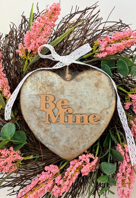 Heart-shaped metal sign with 'Be Mine' text on a floral wreath