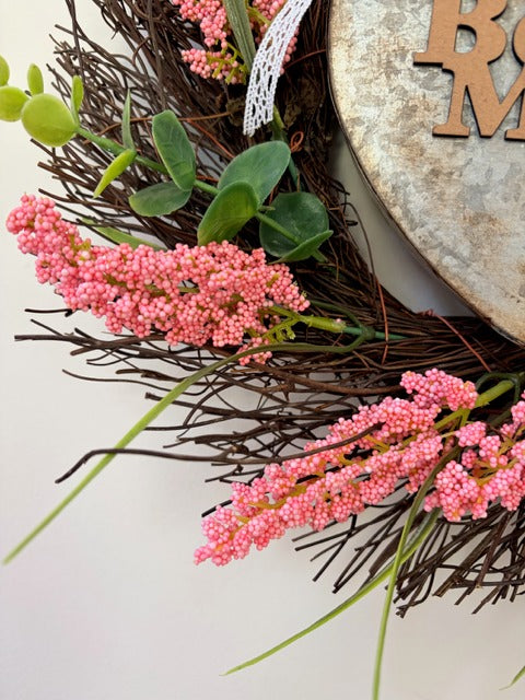 Decorative wreath with pink flowers and green leaves on a white background