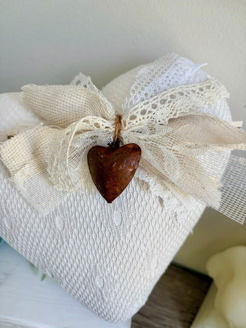 White textured heart with a lace bow and rusty heart ornament on a neutral background