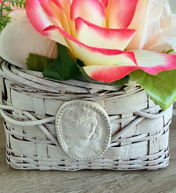 Decorative basket with a clay medallion and pink and white flowers on a wooden surface