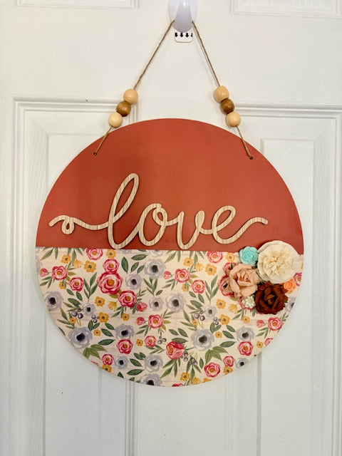 Decorative round sign with floral design and 'love' text on a white door.