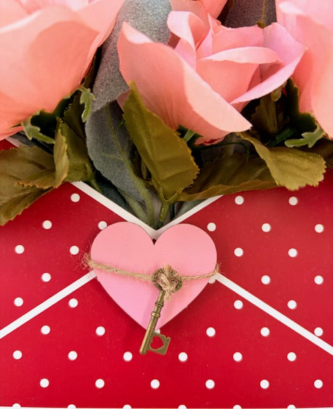 Heart-shaped key charm on a pink heart with pink roses and green leaves on a red polka dot background