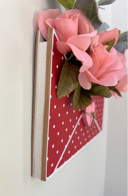 Decorative wall hook with pink flowers and a red polka dot heart on a white background
