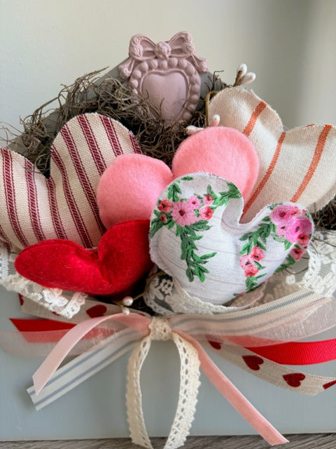 Decorative arrangement of heart-shaped pillows with a floral heart pillow at the center, tied with ribbons.