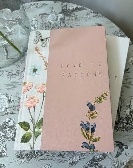 Book with floral design and 'LOVE IS PATIENT' text on a decorative surface.
