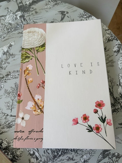 Book with 'Love is Kind' text on a floral-patterned background