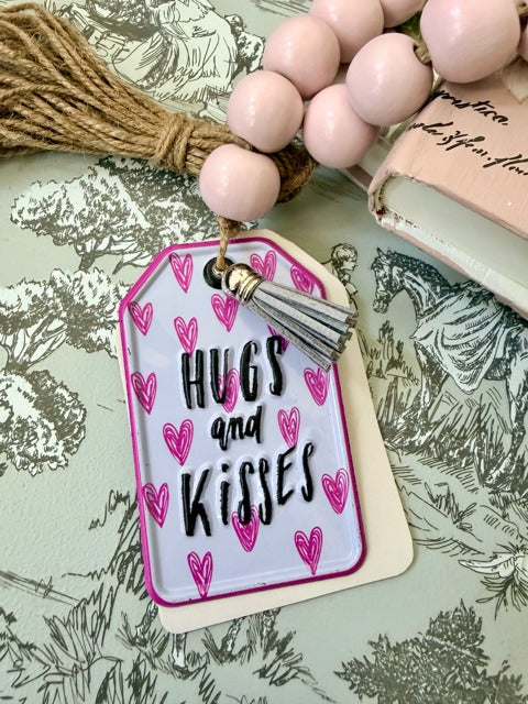 Tag with 'Hugs and Kisses' text and pink hearts, attached to a beaded garland.