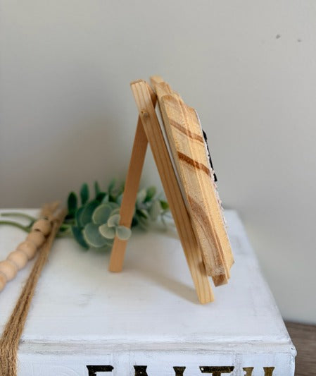 Decorative sign with 'Be Mine' on a floral background with a wooden stand.
