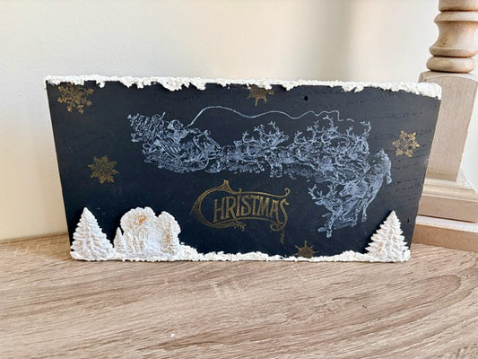 Decorative Christmas block with snowflake and tree designs on a wooden surface.