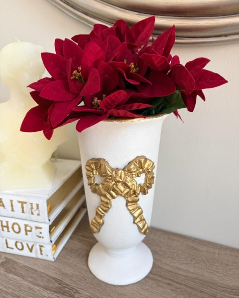 White vase with gold bow design holding red poinsettias 