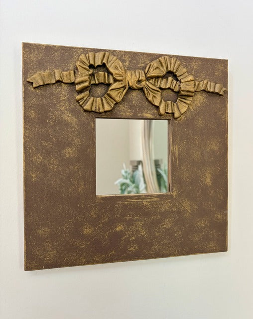 Decorative mirror with gold bow design on a white wall