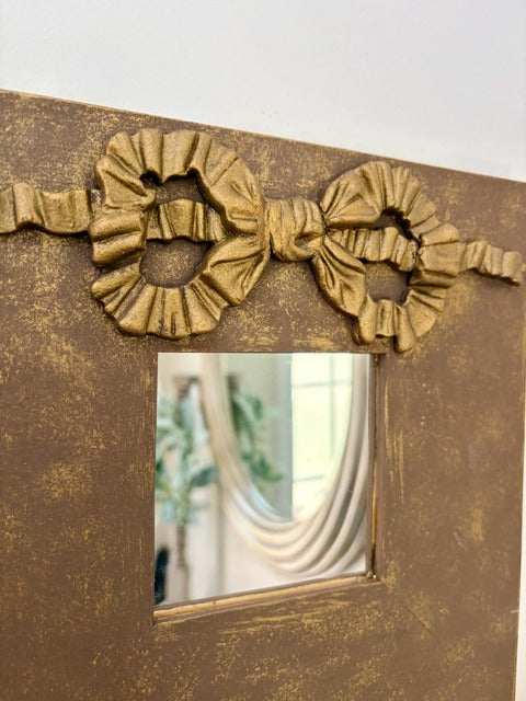 Decorative gold mirror with a bow-like design on a white background
