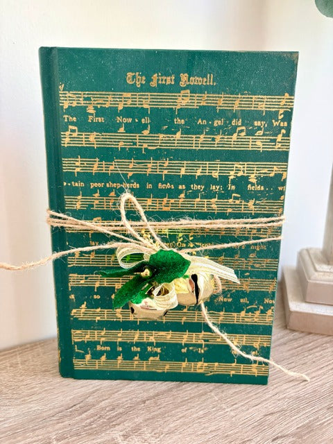 Green book with sheet music design, tied with twine and a decorative bell