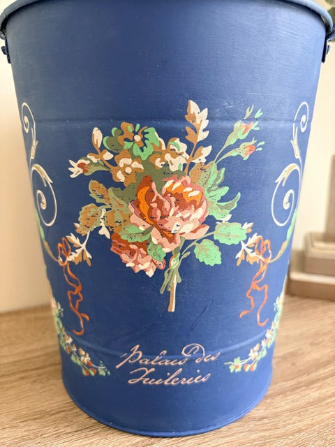 Blue bucket with floral design and 'Palais des Tuileries' text on a wooden surface