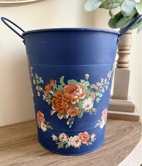 Blue metal bucket with floral design on a wooden surface