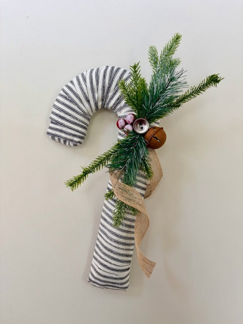 Decorative candy cane with striped fabric, greenery, and a bell on a white background