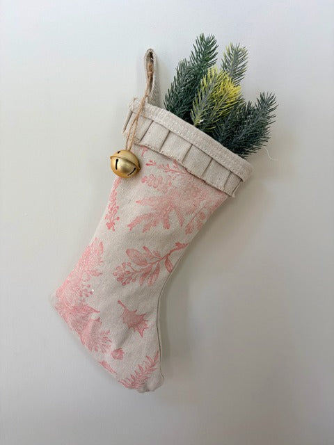 Decorative Christmas stocking with red floral pattern, gold bell, and greenery on a white background
