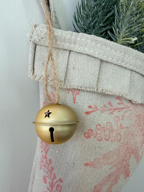 Gold bell hanging on a textured fabric surface with greenery in the background