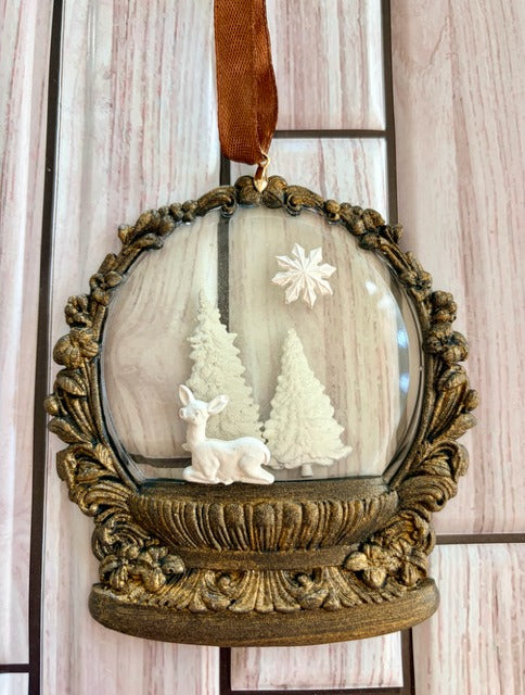 Decorative ornament with deer and trees inside a resin sphere, hanging on a ribbon.