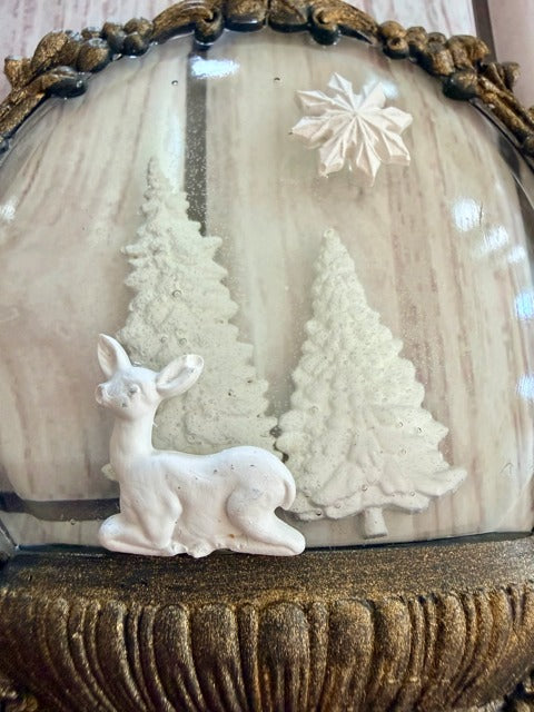 Decorative scene with a deer and trees inside a resin dome with ornate gold frame.
