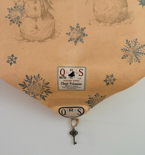 Vintage paper with snowmen and snowflakes, featuring a QRS label and key charm.