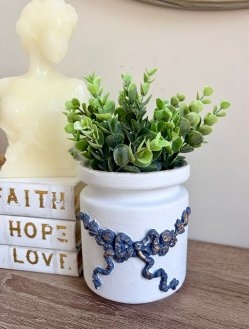 Vase with blue and gold bow, and greenery.