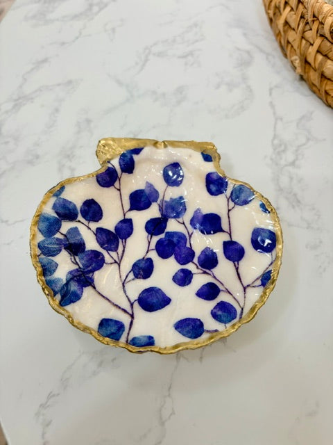 A small decorative dish with an irregular scalloped edge, featuring a floral  pattern on a white background with a gold-toned distressed rim.