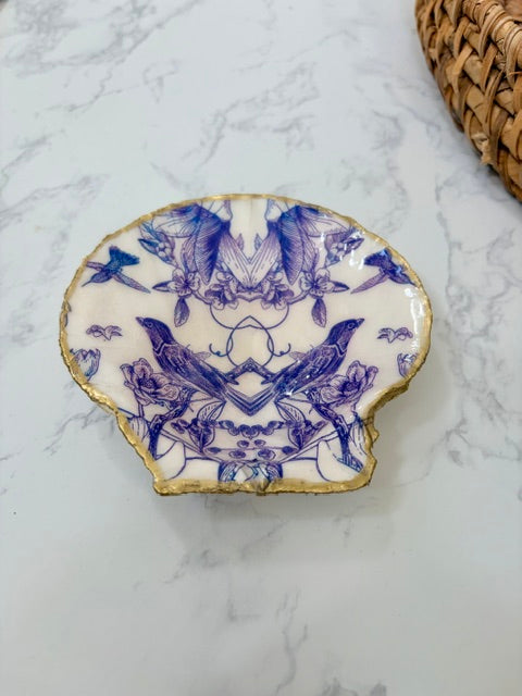 A small decorative dish with an irregular scalloped edge, featuring a floral  pattern with birds on a white background with a gold-toned distressed rim.